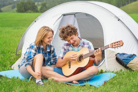 帐篷附近的十几岁男孩和女孩在户外弹吉他
