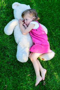 悲伤的小女孩和大泰迪熊躺在草地上