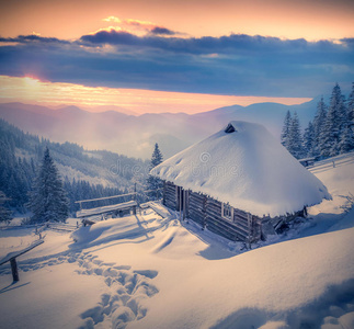 日出时山上覆盖着雪的森林人的小屋。