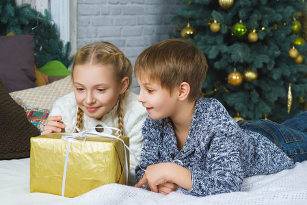 快乐的男孩和女孩躺在床上。旁边的礼物。在等待圣诞节。庆祝活动。新的一年
