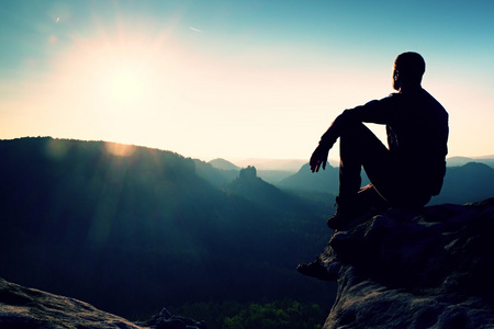 旅游休息。英俊的年轻男子坐在岩石上享受着成雾落矶山脉的景色