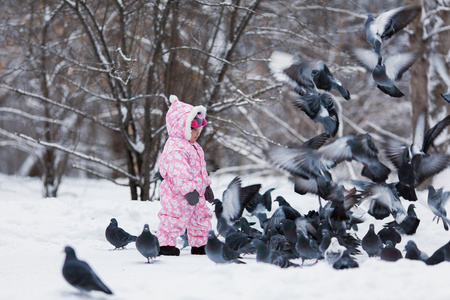 漂亮的小女孩喂鸟在冬天雪园