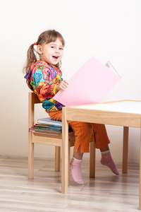 快乐的女孩坐在一摞书在桌子上
