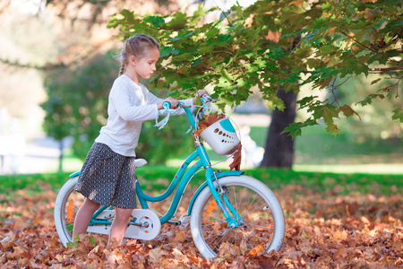 可爱女孩骑着一辆自行车在温暖的秋日户外活动