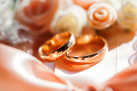 金色钻石婚戒躺在真丝织物上玫瑰。爱情和婚姻的象征