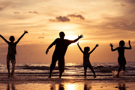 父亲和孩子们在日落的时候在海滩上玩