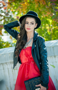 美丽的女人，与在秋季公园构成的黑帽子。花时间在秋天期间在森林的年轻黑妞。长头发迷人创意化妆和红色连衣裙的女孩，在户外拍摄在秋天