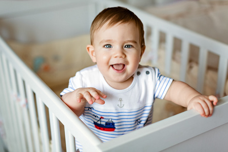 小可爱小可爱金发的男孩，在条纹的大包围是在育儿室，白色的婴儿床和笑