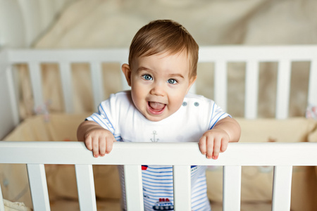 小可爱小可爱金发的男孩，在条纹的大包围是在育儿室，白色的婴儿床和笑