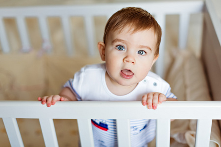 小可爱小可爱金发的男孩，在条纹的大包围是在育儿室，白色的婴儿床和持有的句柄