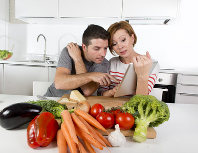 美国夫妇在国内厨房妻子后食谱在数字垫与丈夫一起工作