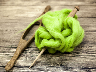 绿色的羊毛和老主轴特写木制背景上。羊毛针织的工具