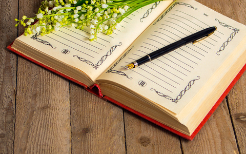 白色的波斯毛茛花玉兰花用的书和钢笔提醒婚礼日在日历规划和钢笔与