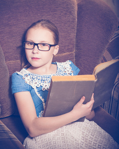 在家里读书的女孩坐在扶手椅上