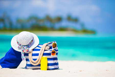 蓝色的袋子，秸秆白帽子 墨镜和防晒霜瓶热带海滩上