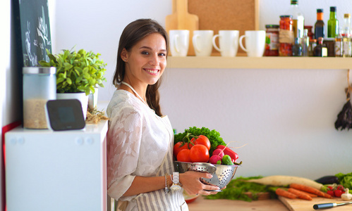 微笑的年轻女子捧着站在厨房里的蔬菜