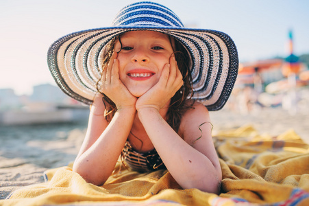快乐的孩子在夏天海滩上放松的泳装，躺在毛巾上，得到一些潭。温暖的天气，放松心情。在暑假旅行。选择性的焦点