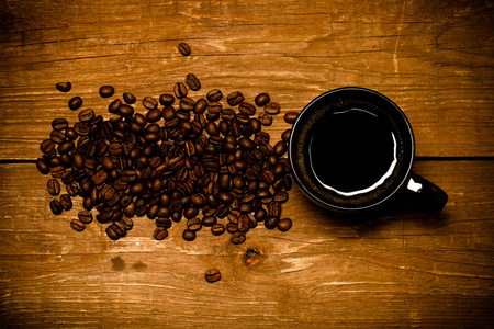 咖啡和咖啡种子在旧木桌上的黑色茶杯。定了调子