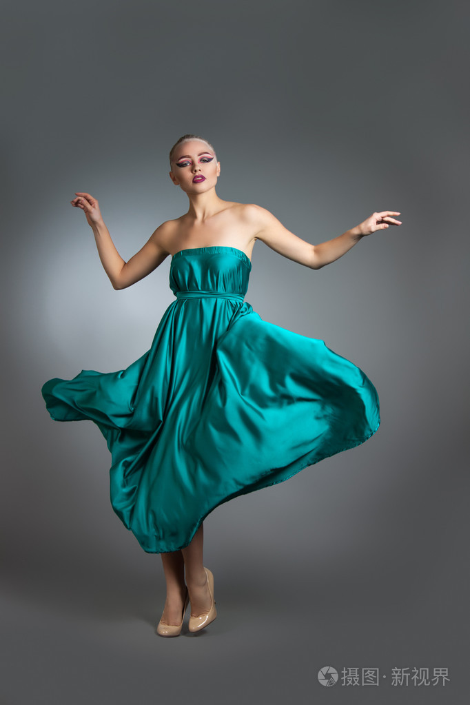 在风中挥舞着的丝绸衣服的女人.飞行和飘飘礼服布在灰色的背景