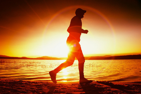 赛跑者在太阳光线在海滩上。运动员戴棒球帽，慢跑在以上海上日出