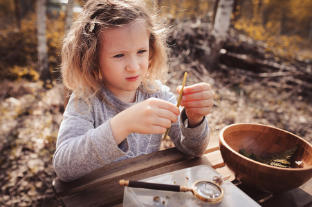 儿童女孩在早春，探索自然看着第一芽苗菜用放大镜。教孩子们爱自然