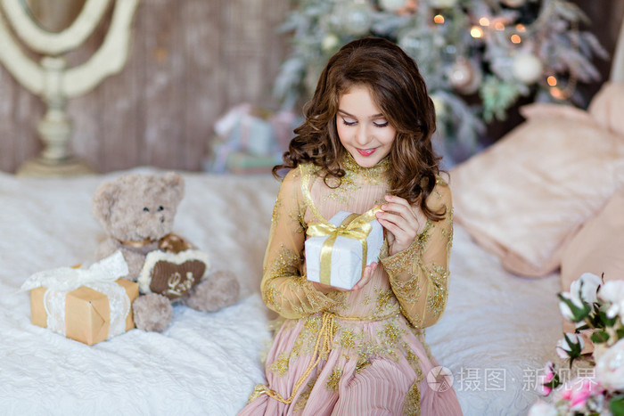 年轻漂亮卷发的女孩打开礼物在圣诞树上