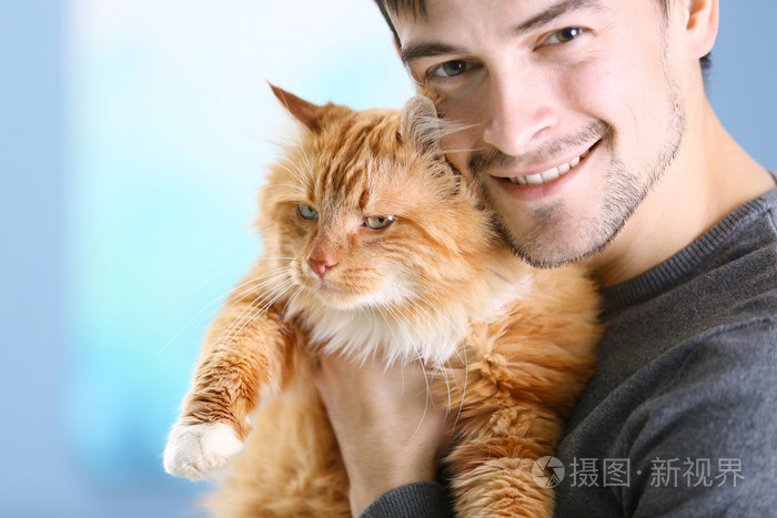 年轻的男人微笑着抱着毛茸茸的红色只猫