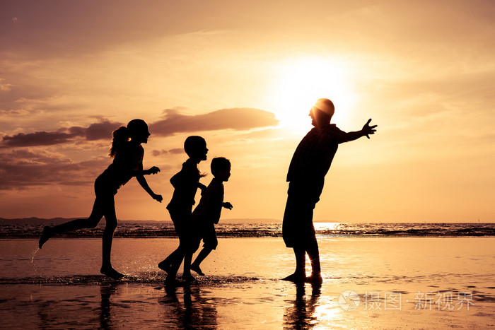 父亲和孩子们在日落的时候在海滩上玩