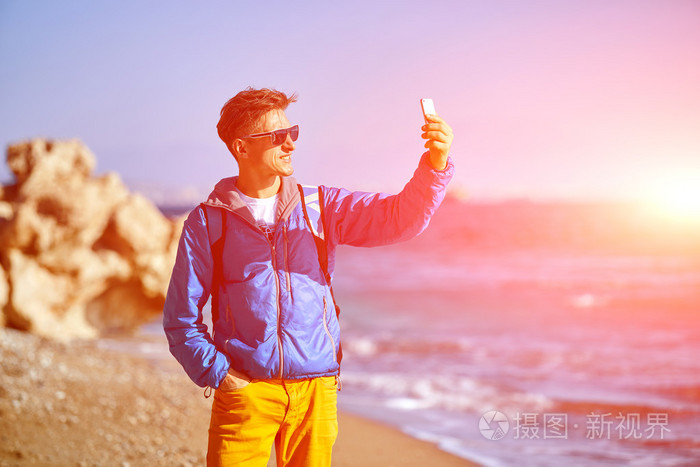 旅行者带着背包,在清晨的海面和蓝天上自拍
