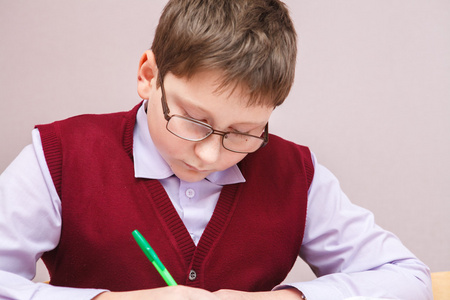 小学生近视小男孩戴着眼镜坐在桌子上写作照片