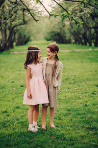 在春天的花园里，两个快乐考究小女友拥抱室外。孩子姐妹花时间在一起散步
