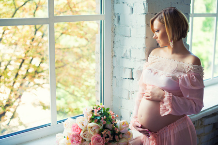 靠近窗户的怀孕女孩。快乐的健康怀孕。等待的宝贝