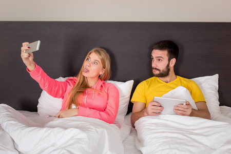 年轻的幸福夫妇在床上用电话相机自拍。
