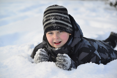 小男孩躺在冬季的森林里的雪