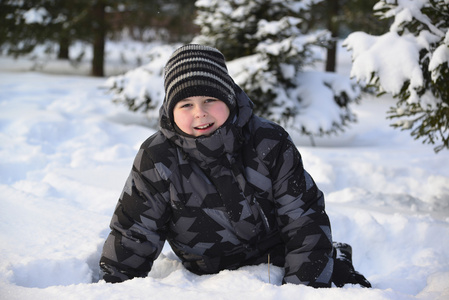 十几岁的小男孩坐在冬季的森林里的雪