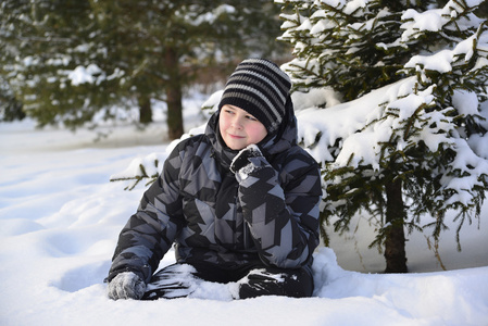 十几岁的小男孩坐在冬季的森林里的雪