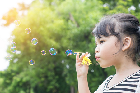 亚洲小女孩吹肥皂泡的绿色公园