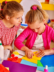 孩子们在幼儿园的桌子上拿着彩色纸。