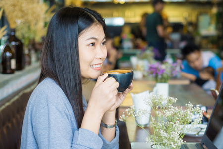 女人在咖啡店用笔记本电脑喝拿铁。