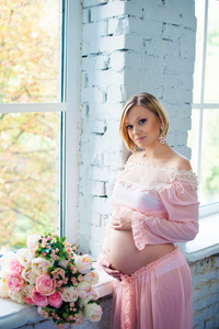 怀孕的女孩，抱着肚子在窗口附近。快乐 9 个月的怀孕并等待生