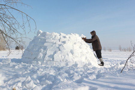 男子在冬天建立在雪林间空地上的一座冰屋