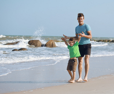 幸福的家庭，在海滩玩，父亲与儿子步行的海洋海岸岩石背后微笑享受夏天