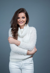 肖像年轻漂亮的女孩微笑，穿着白色的针织的毛衣，灰色的背景上孤立