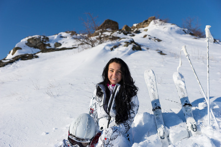 女滑雪者坐在白雪皑皑的山坡上，与滑雪板