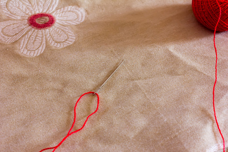 缝针线程模式线程被通过一根针和一个红色的毛线球亚麻织物的一种模式
