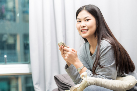 年轻女子在床上使用智能手机，背景是窗帘和窗户