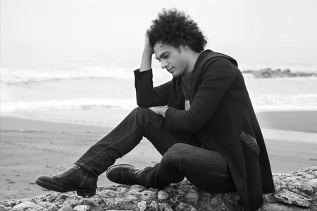 悲伤孤独的人坐在海洋前用在黑色和白色的冬天画像中的波浪