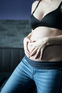 怀孕的女人抱着她的肚子随着方便形成一颗心