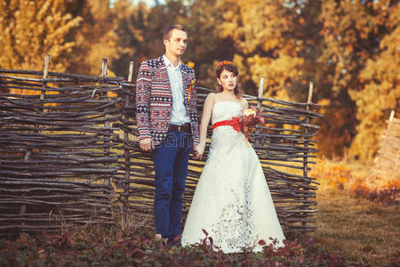 新郎新娘手牵着手站在柳条篱笆旁