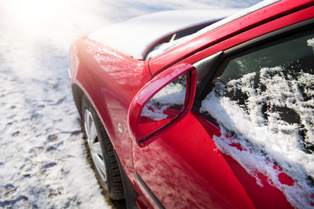 雪覆盖的红色汽车停在外面，重点放在后视镜，冬季运输问题
